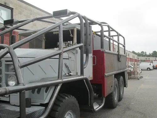 Exterior view of small fire truck showing cab, body compartments, and wheel/tire area.