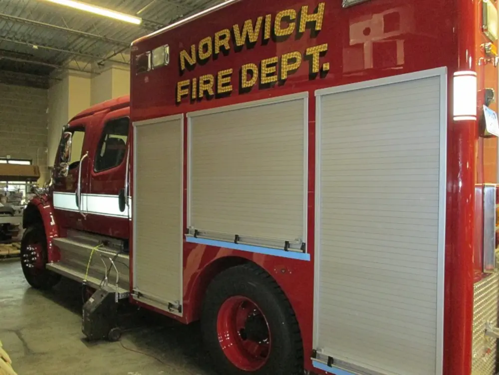 Exterior view of small fire truck showing cab, body compartments, and wheel/tire area.