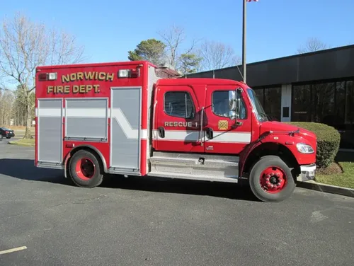 Exterior view of small fire truck showing cab, body compartments, and wheel/tire area.