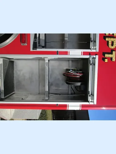 Exterior view of small fire truck showing cab, body compartments, and wheel/tire area.
