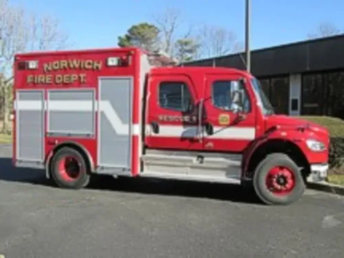 Exterior view of small fire truck showing cab, body compartments, and wheel/tire area.