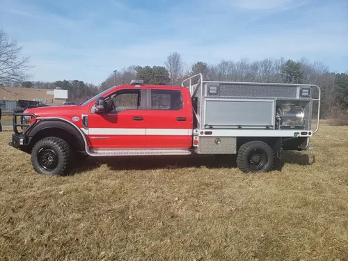 Exterior view of small fire truck showing cab, body compartments, and wheel/tire area.