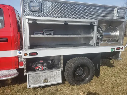 Exterior view of small fire truck showing cab, body compartments, and wheel/tire area.