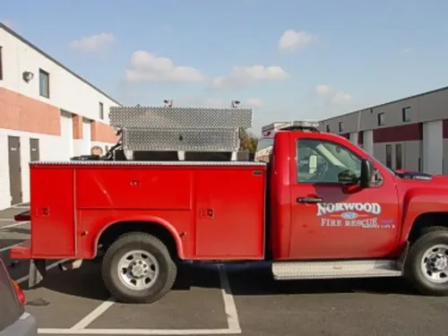 Exterior view of small fire truck showing cab, body compartments, and wheel/tire area.