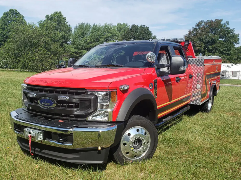 Exterior view of small fire truck showing cab, body compartments, and wheel/tire area.