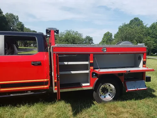 Exterior view of small fire truck showing cab, body compartments, and wheel/tire area.