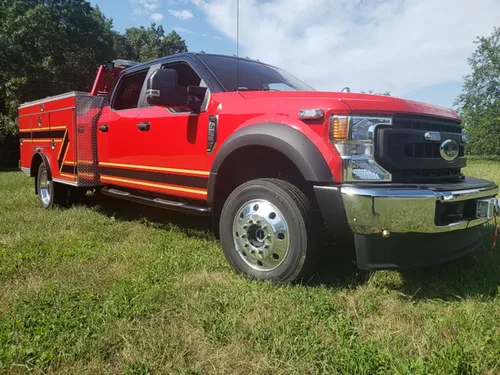 Exterior view of small fire truck showing cab, body compartments, and wheel/tire area.