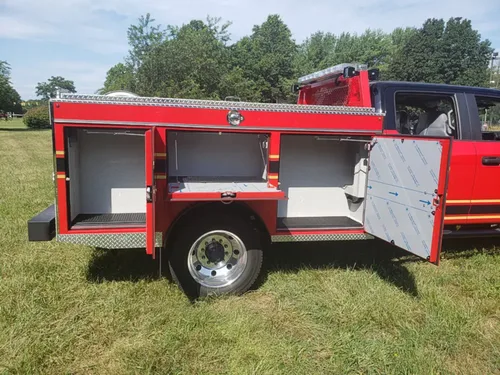Exterior view of small fire truck showing cab, body compartments, and wheel/tire area.