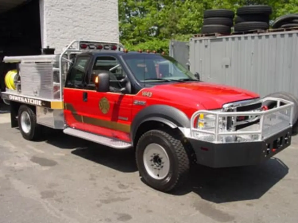 Exterior view of small fire truck showing cab, body compartments, and wheel/tire area.