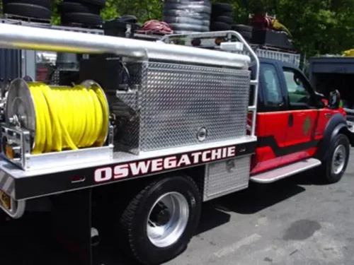 Exterior view of small fire truck showing cab, body compartments, and wheel/tire area.