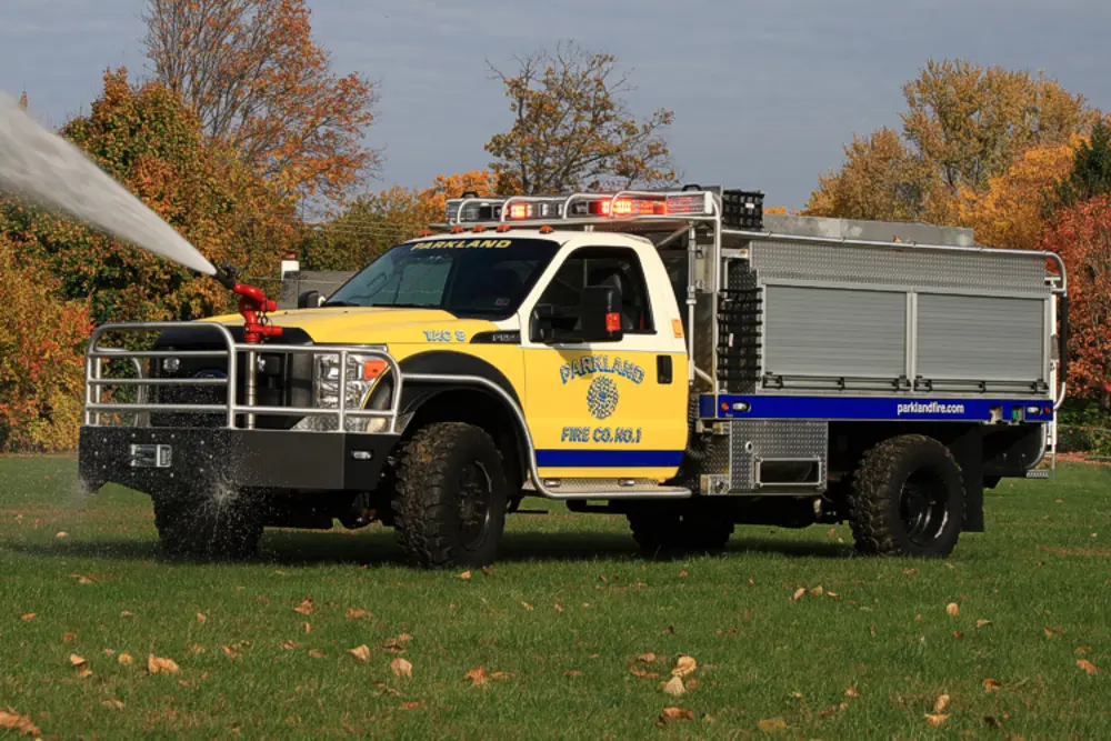 Exterior view of small fire truck showing cab, body compartments, and wheel/tire area.
