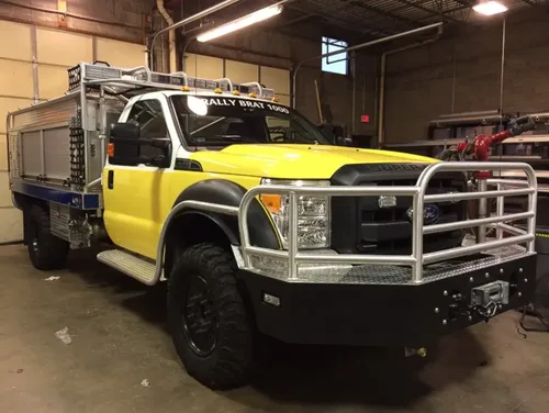 Exterior view of small fire truck showing cab, body compartments, and wheel/tire area.