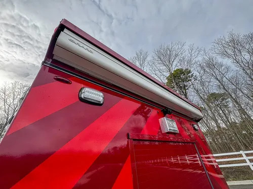 Exterior view of small fire truck showing cab, body compartments, and wheel/tire area.