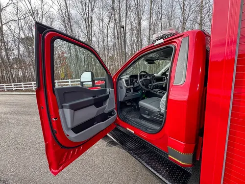 Exterior view of small fire truck showing cab, body compartments, and wheel/tire area.