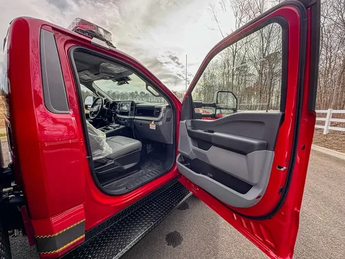 Exterior view of small fire truck showing cab, body compartments, and wheel/tire area.