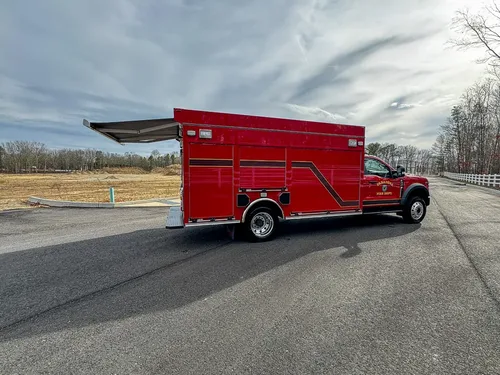 Exterior view of small fire truck showing cab, body compartments, and wheel/tire area.
