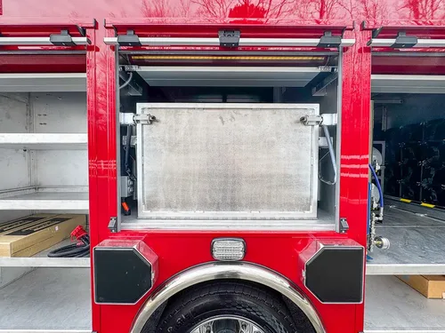 Exterior view of small fire truck showing cab, body compartments, and wheel/tire area.