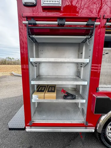 Exterior view of small fire truck showing cab, body compartments, and wheel/tire area.
