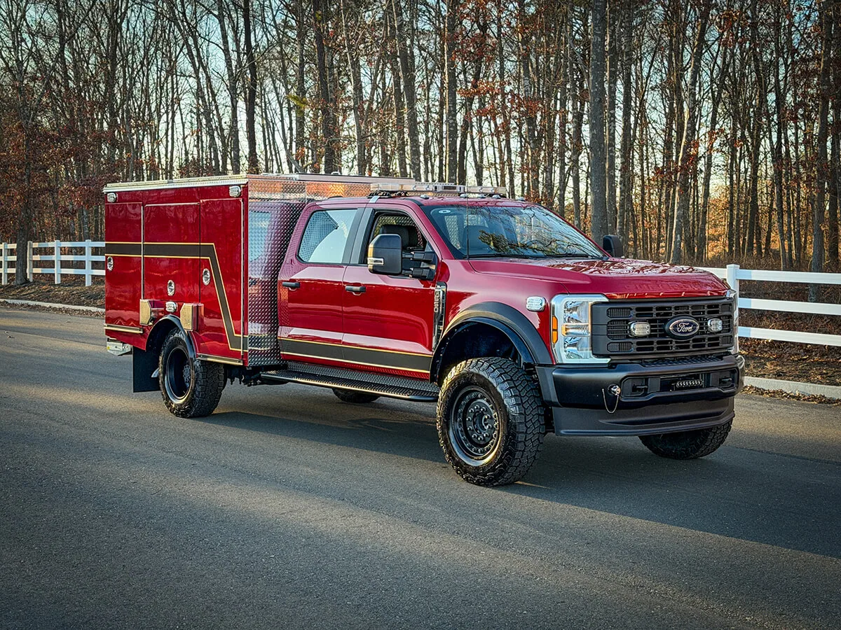 Red brush truck in front three-quarter view on a paved road.