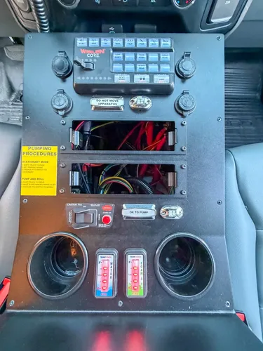 Top-down close-up of center console with switches, cup holders, and open wiring bays.