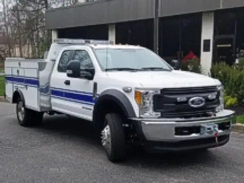 Exterior view of small fire truck showing cab, body compartments, and wheel/tire area.