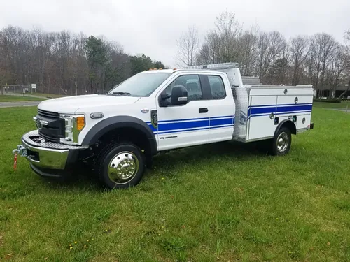 Exterior view of small fire truck showing cab, body compartments, and wheel/tire area.
