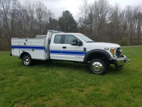 Exterior view of small fire truck showing cab, body compartments, and wheel/tire area.