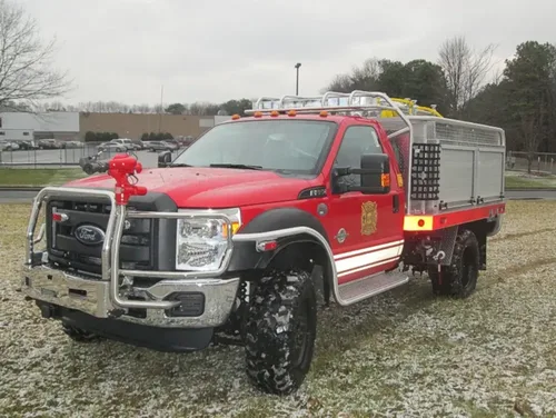 Exterior view of small fire truck showing cab, body compartments, and wheel/tire area.