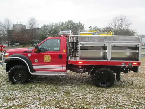 Exterior view of small fire truck showing cab, body compartments, and wheel/tire area.