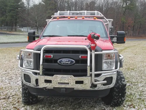 Exterior view of small fire truck showing cab, body compartments, and wheel/tire area.
