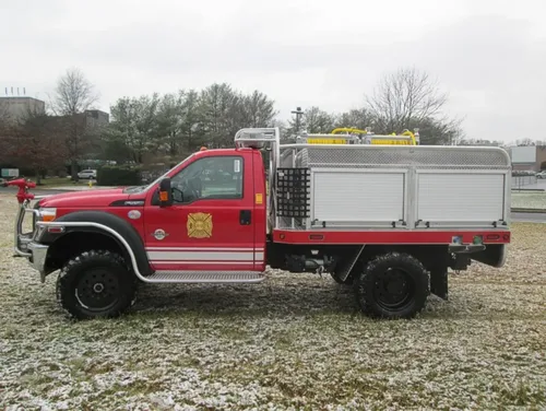 Exterior view of small fire truck showing cab, body compartments, and wheel/tire area.