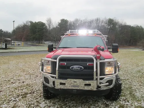 Exterior view of small fire truck showing cab, body compartments, and wheel/tire area.