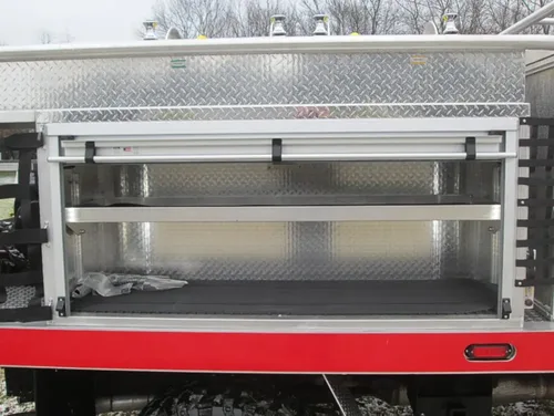 Exterior view of small fire truck showing cab, body compartments, and wheel/tire area.