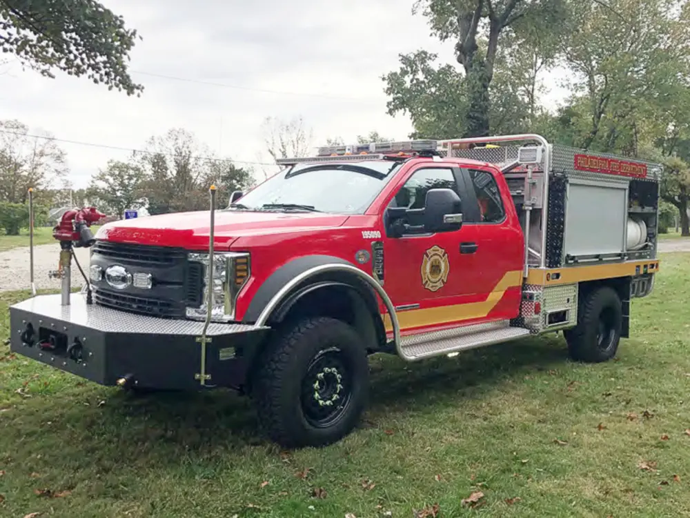 Exterior view of small fire truck showing cab, body compartments, and wheel/tire area.
