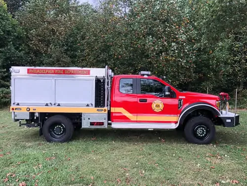 Exterior view of small fire truck showing cab, body compartments, and wheel/tire area.