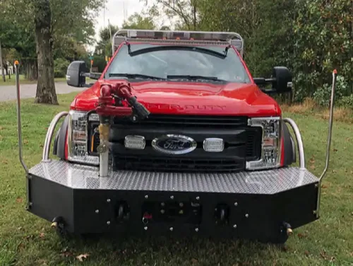 Exterior view of small fire truck showing cab, body compartments, and wheel/tire area.