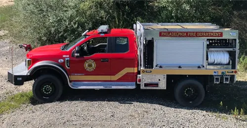 Exterior view of small fire truck showing cab, body compartments, and wheel/tire area.