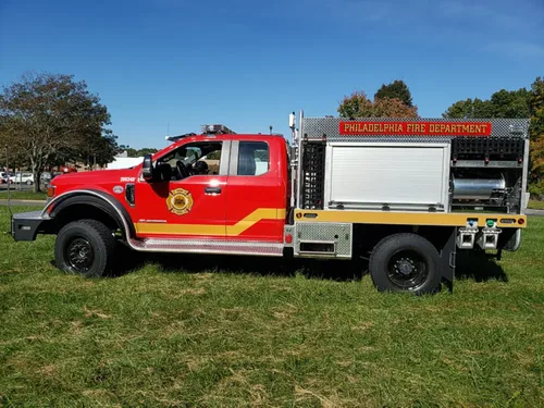 Exterior view of small fire truck showing cab, body compartments, and wheel/tire area.