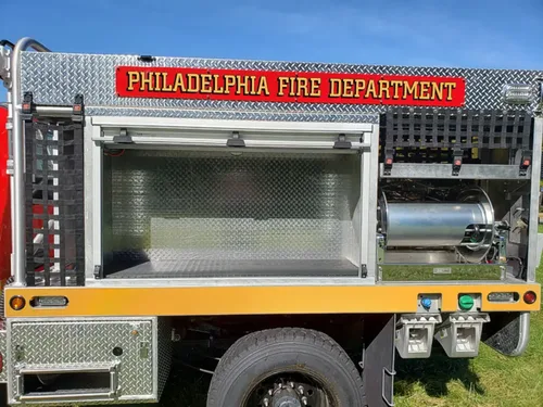 Exterior view of small fire truck showing cab, body compartments, and wheel/tire area.