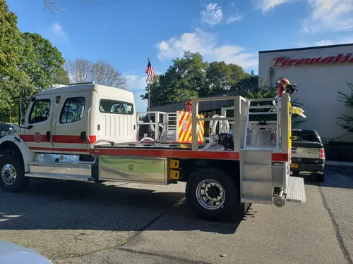 Exterior view of small fire truck showing cab, body compartments, and wheel/tire area.