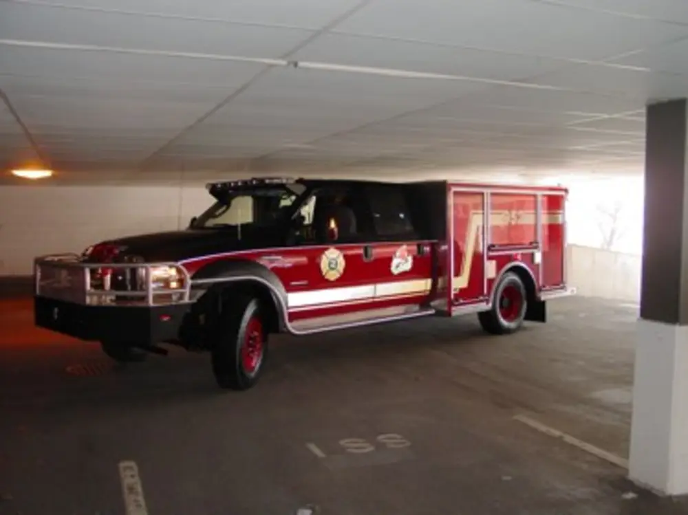 Exterior view of small fire truck showing cab, body compartments, and wheel/tire area.