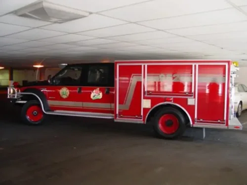 Exterior view of small fire truck showing cab, body compartments, and wheel/tire area.