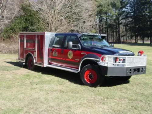 Exterior view of small fire truck showing cab, body compartments, and wheel/tire area.