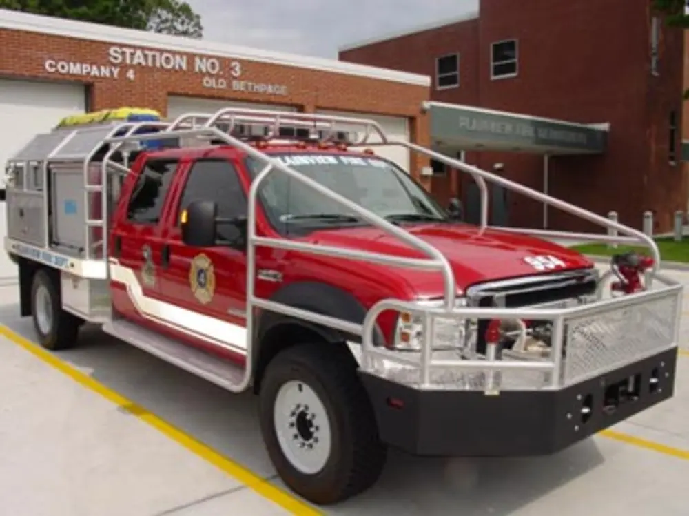 Exterior view of small fire truck showing cab, body compartments, and wheel/tire area.