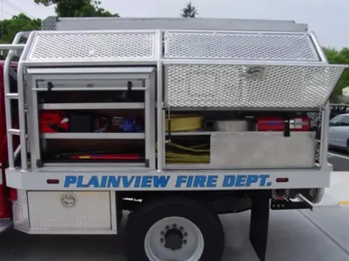 Exterior view of small fire truck showing cab, body compartments, and wheel/tire area.