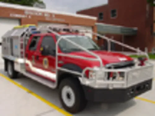 Exterior view of small fire truck showing cab, body compartments, and wheel/tire area.