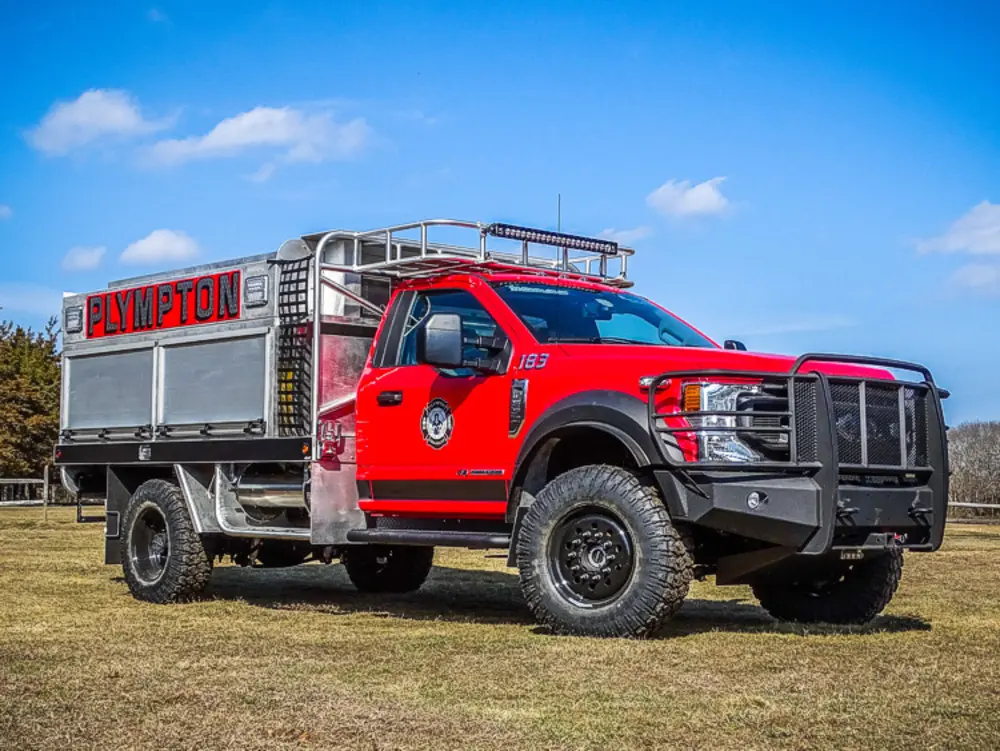Exterior view of small fire truck showing cab, body compartments, and wheel/tire area.