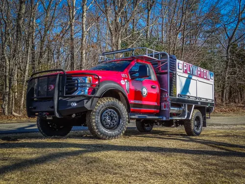 Exterior view of small fire truck showing cab, body compartments, and wheel/tire area.