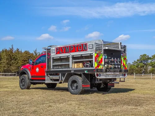 Exterior view of small fire truck showing cab, body compartments, and wheel/tire area.