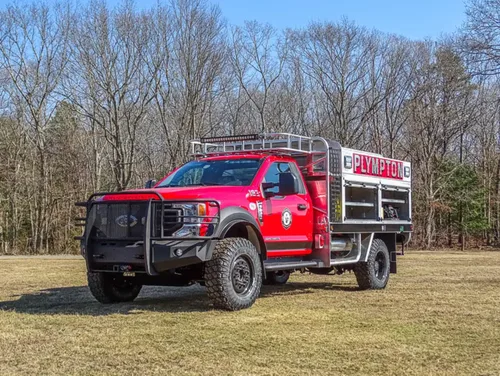 Exterior view of small fire truck showing cab, body compartments, and wheel/tire area.